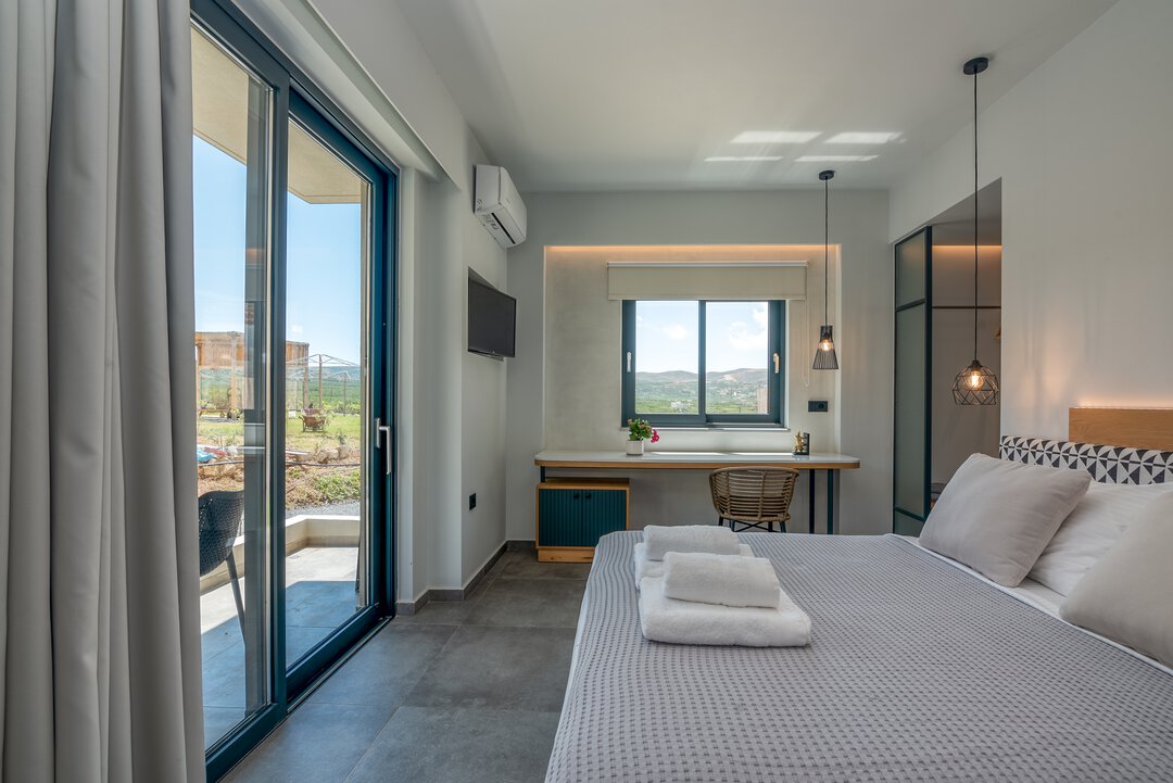 Modern bedroom with king bed, geometric headboard, sliding doors to balcony with sea views at Nusa Falassarna, Crete