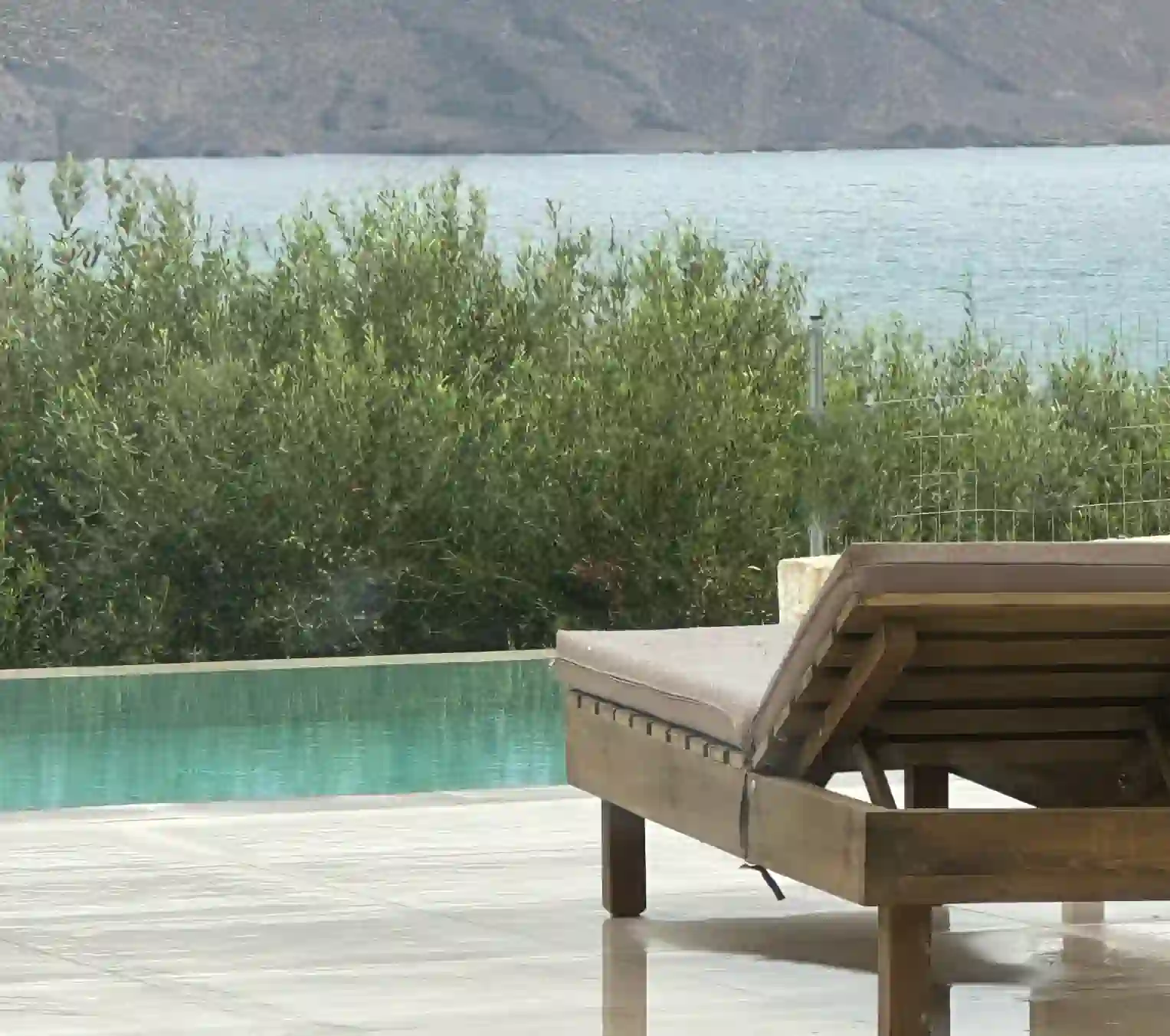Teak sun lounger by turquoise infinity pool with olive grove and sea views at Nusa Retreat, Kissamos, Crete